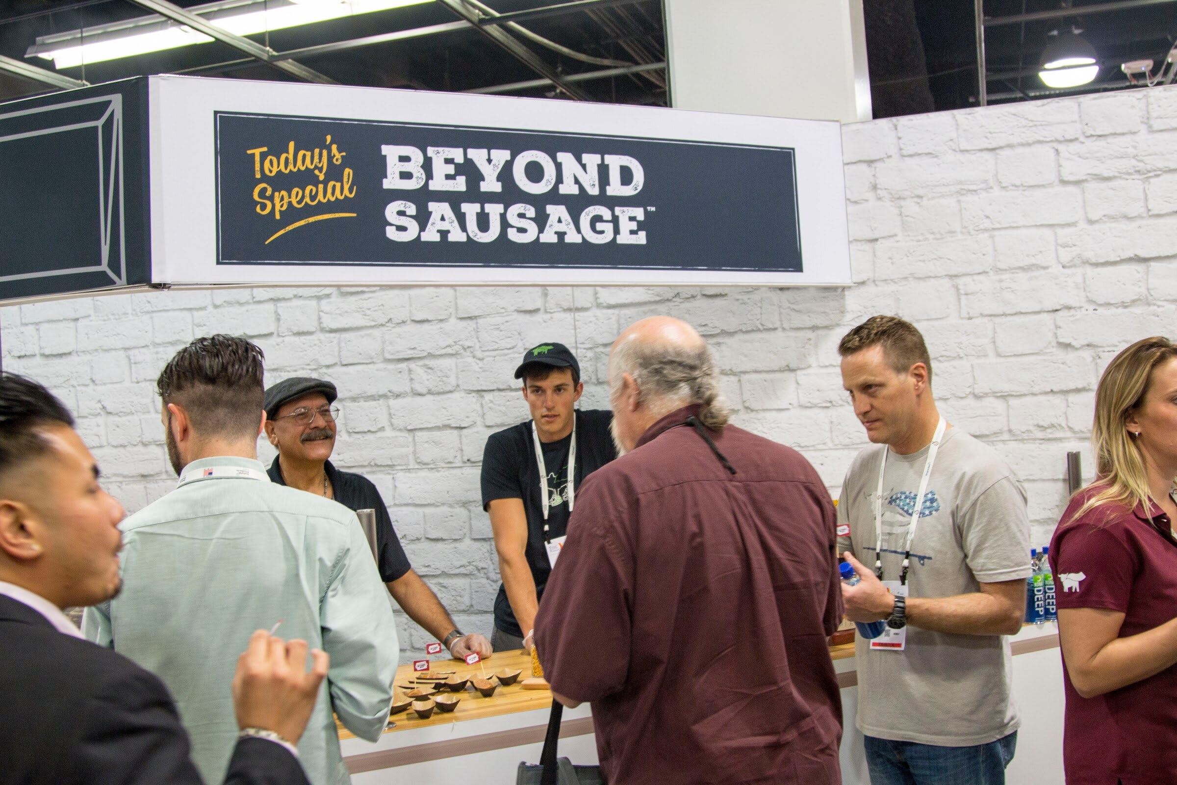 Crowd at a white-brick booth under a sign reading 'Today's Special Beyond Sausage' with staff handing out samples.
