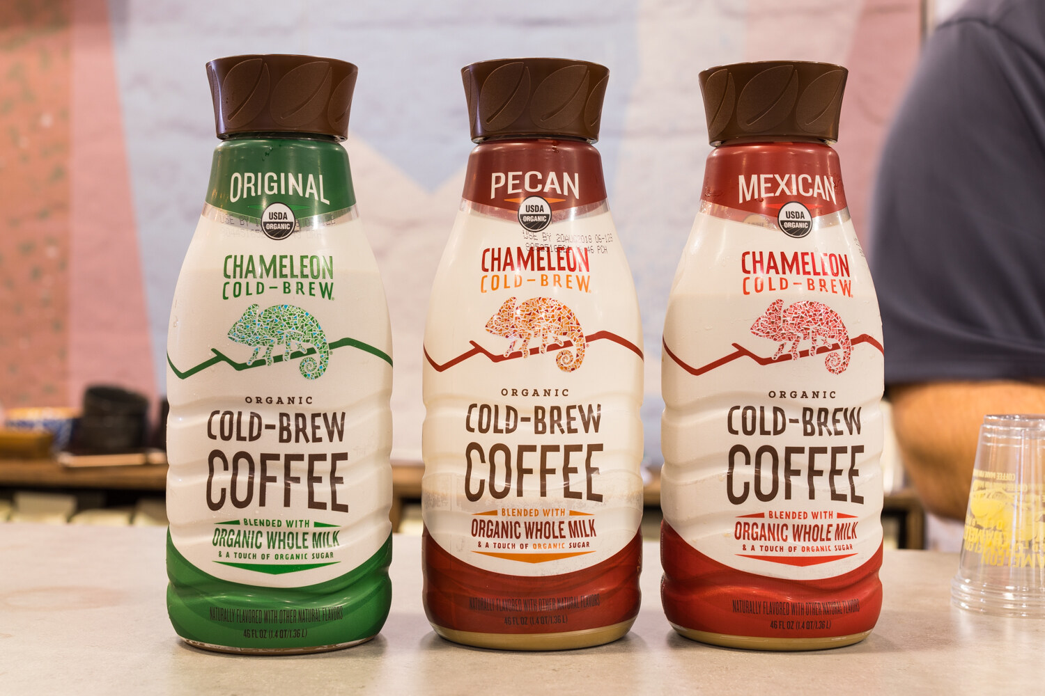 Three bottles of Chameleon Organic Cold-Brew Coffee with brown caps and chameleon illustrations.