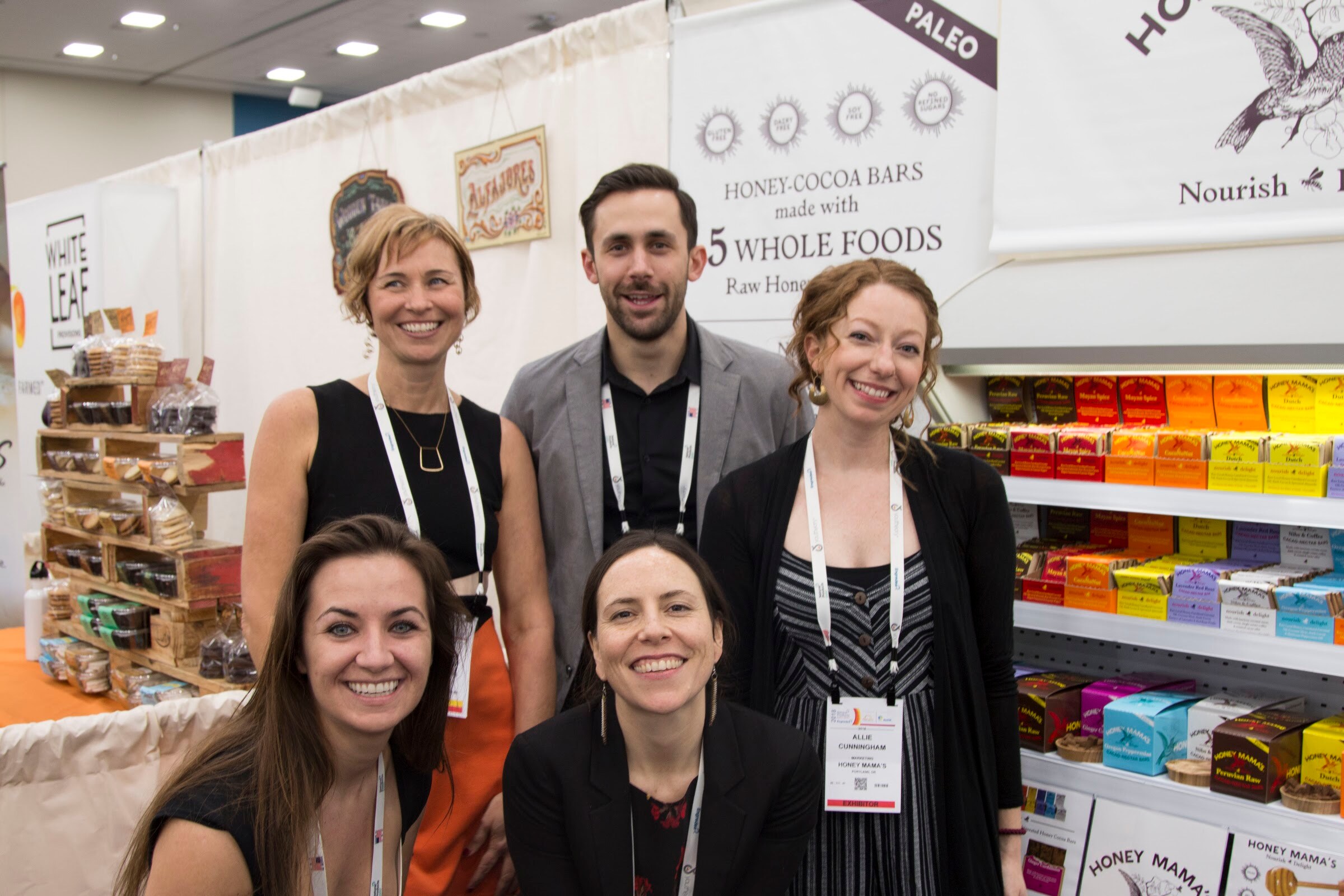 Group of five exhibitors with badges standing together in front of shelves of boxed bars labelled Honey Mama's.