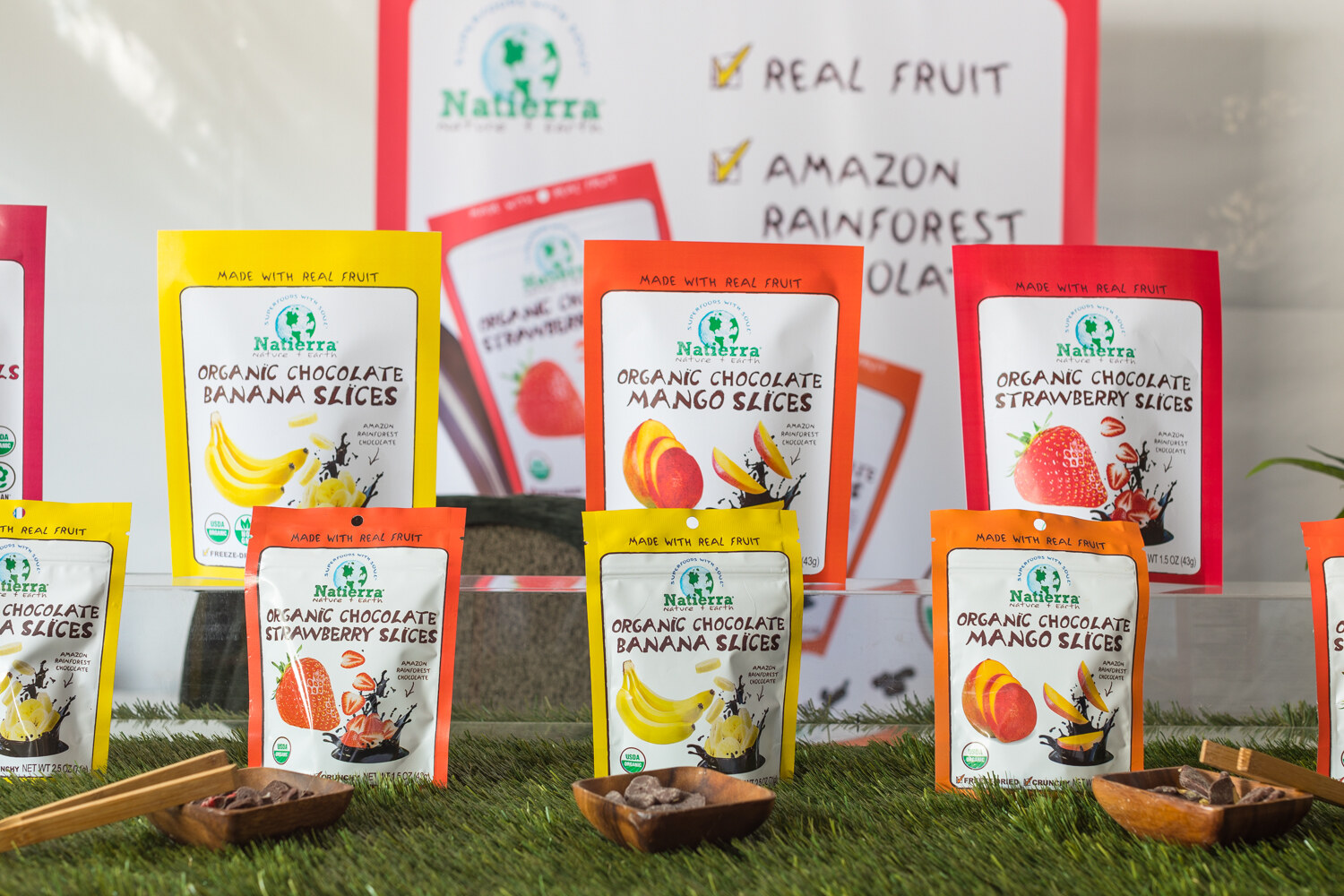 Display of Natierra organic chocolate banana, mango and strawberry slices in yellow, orange and red bags, with a sign reading 'Real fruit, Amazon rainforest'.