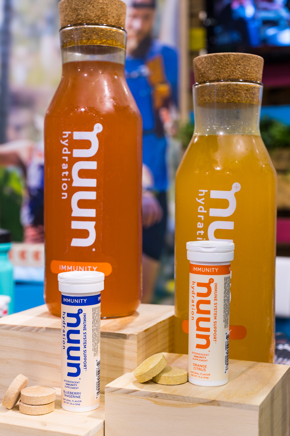 Tall corked bottles of orange and yellow hydration drink labelled nuun with immunity tablet tubes and loose tablets on wooden blocks.