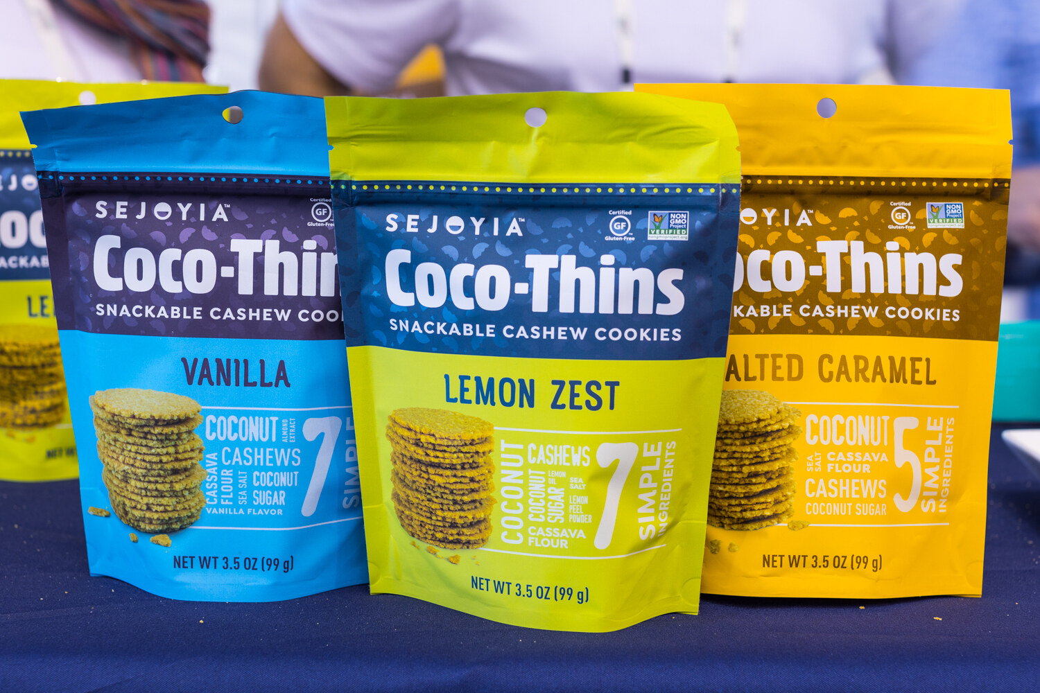 Bags of Sejoyia Coco-Thins in vanilla, lemon zest and salted caramel flavors on a navy tablecloth.