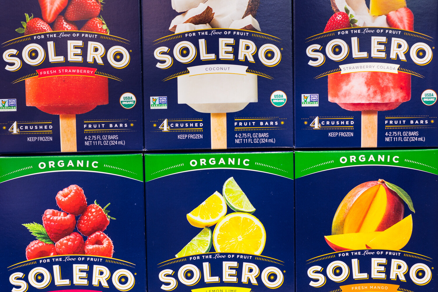 Stack of blue Solero fruit bar boxes showing strawberry, coconut, strawberry colada, raspberry, lemon-lime and mango.
