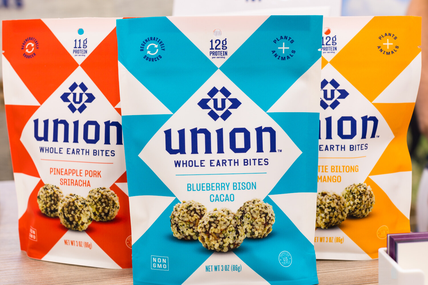Pouches of Union Whole Earth Bites with a blue and white geometric design, showing round snack bites in front.