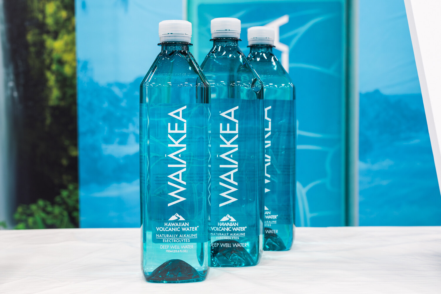 Three tall teal Waiakea bottles on a white counter with a blue backdrop.