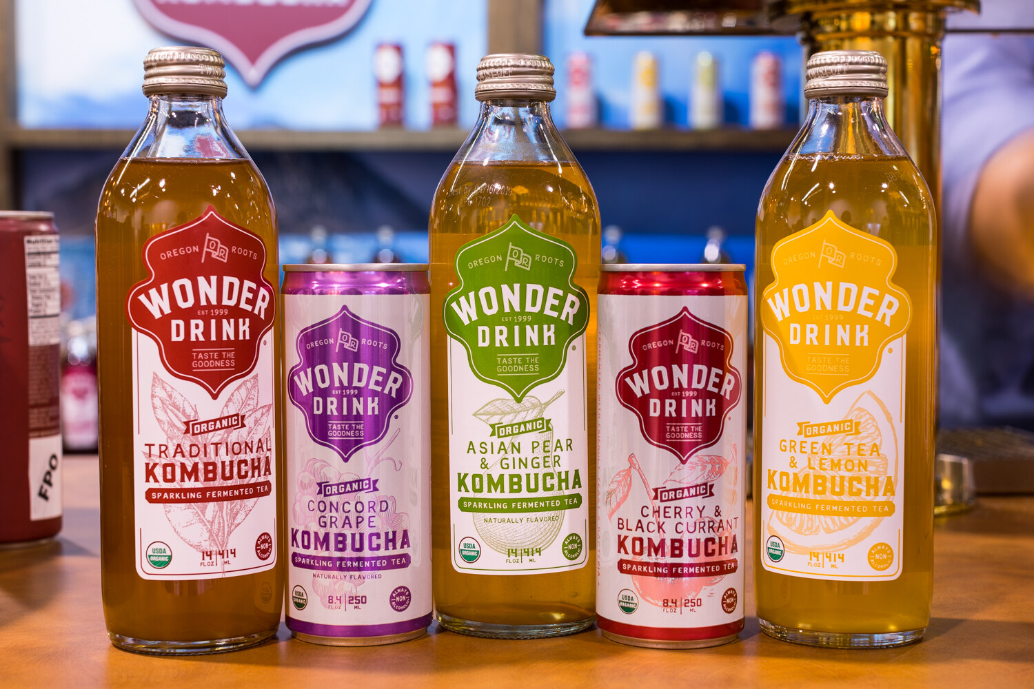 Row of Wonder Drink kombucha bottles and cans in traditional, Concord grape, Asian pear and ginger, cherry and black currant, and green tea and lemon.