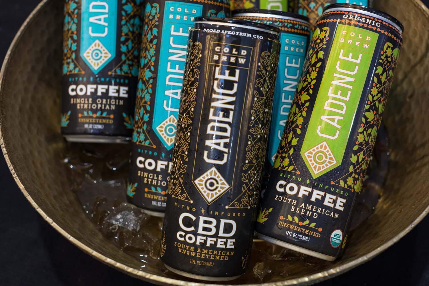Slim black, teal and green Cadence cans in a hammered metal bowl with ice.
