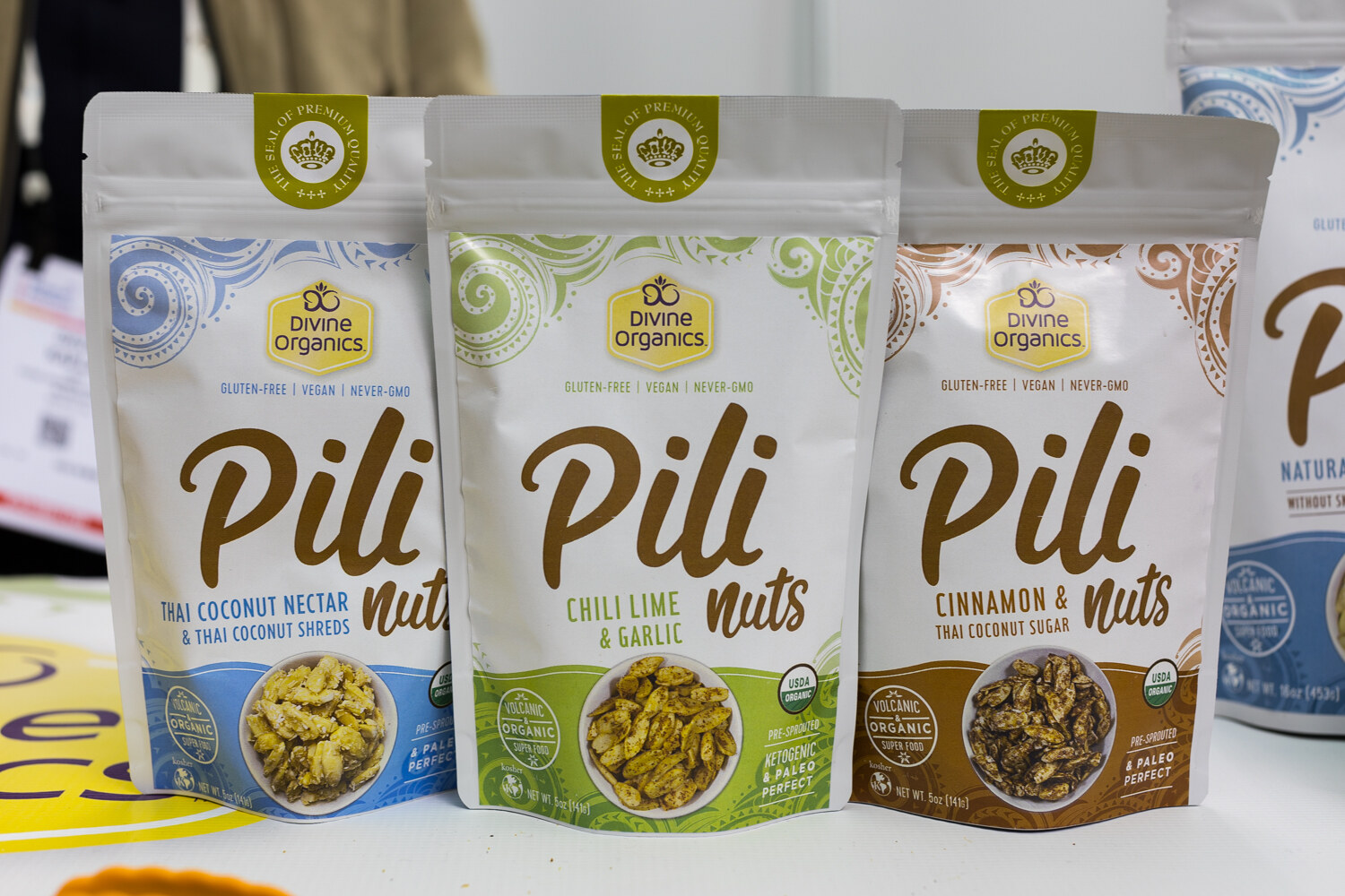 Three white Divine Organics Pili Nuts pouches standing side by side on a white counter.