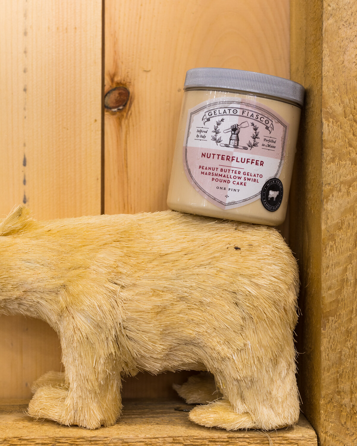 A white pint tub atop a cream-colored straw bear in a wooden crate corner.