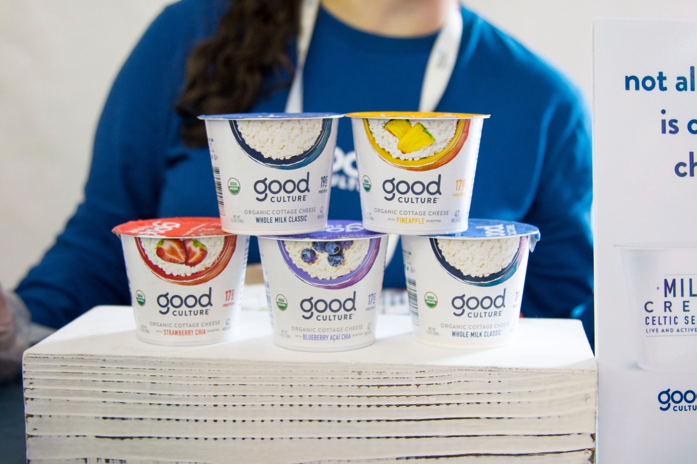 Five Good Culture cups piled on a pedestal with a staffer in a blue shirt and lanyard behind them.