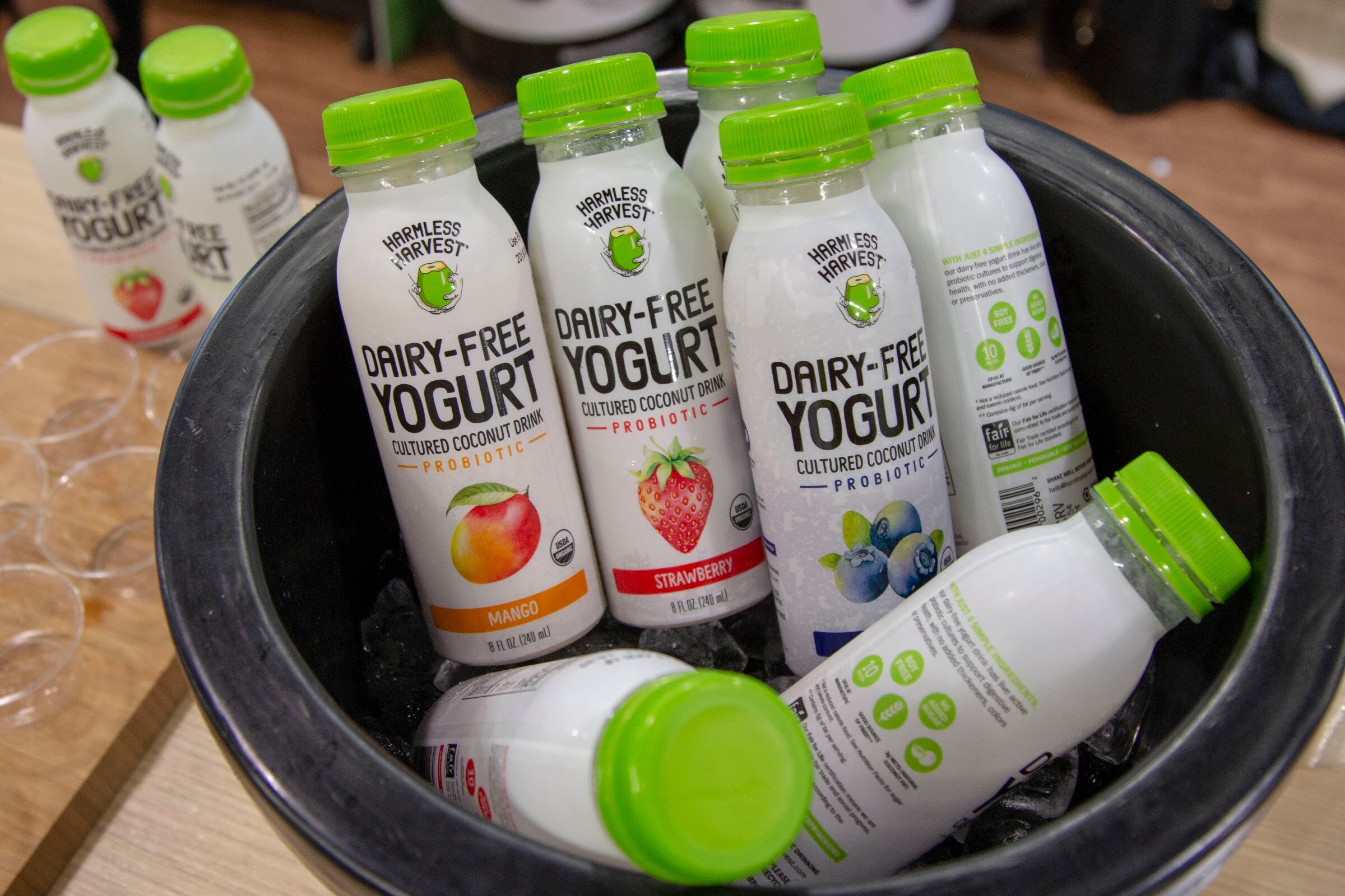 Bottles with green caps in a black bucket among clear sample cups.