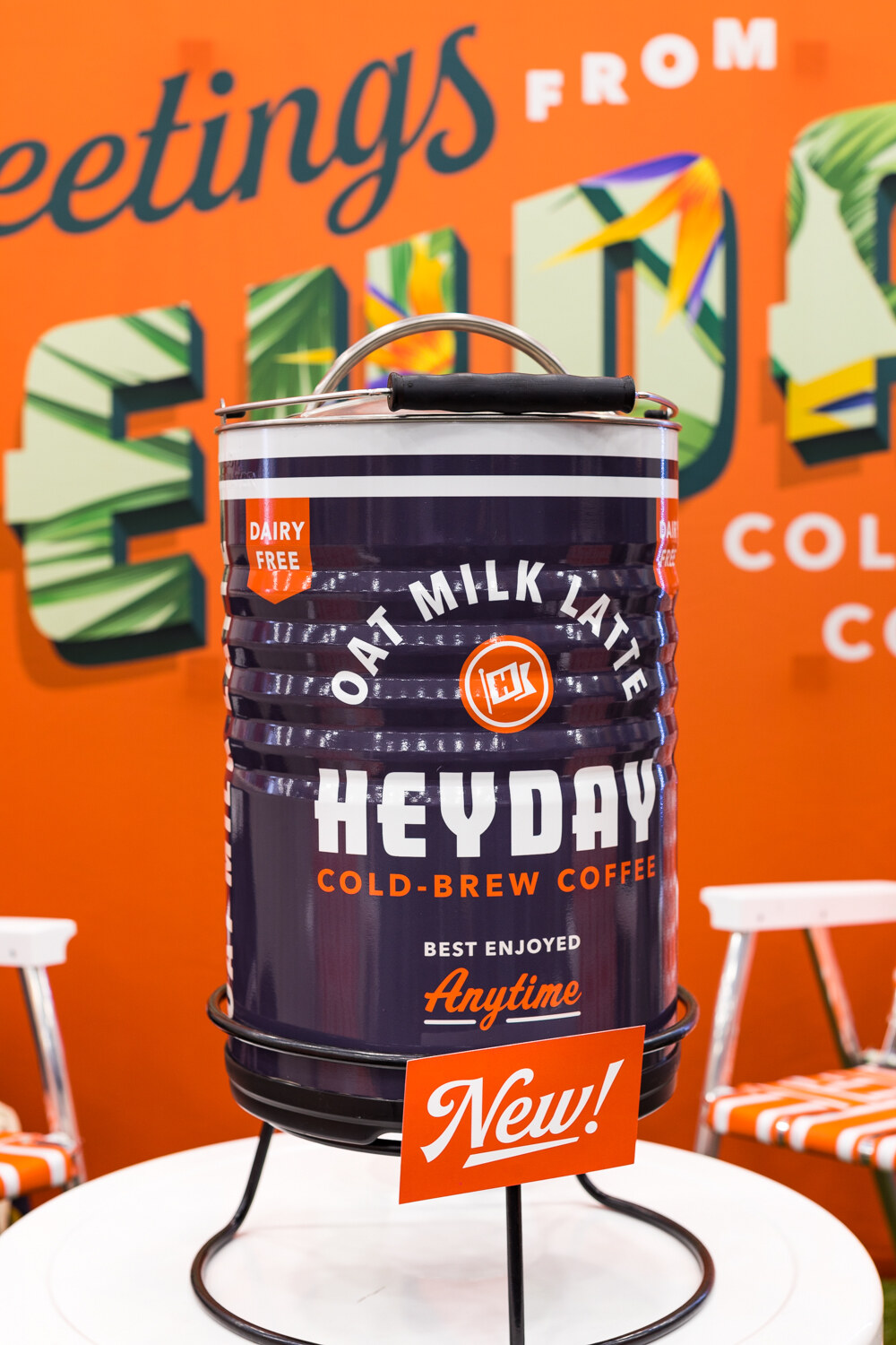 A purple and white Heyday dispenser with a New sign on a white pedestal in front of a bright orange wall mural.