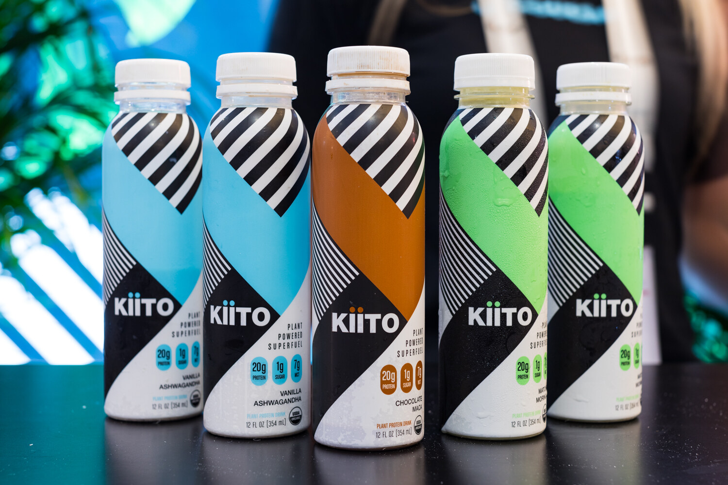 Five Kiito bottles with black and white diagonal stripes in blue, brown and green on a black counter.