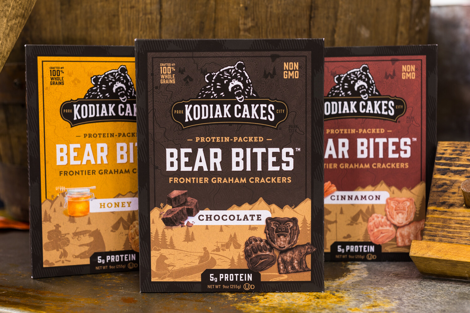 Three boxes of Kodiak Cakes Bear Bites in yellow, brown and red against old wood planks.