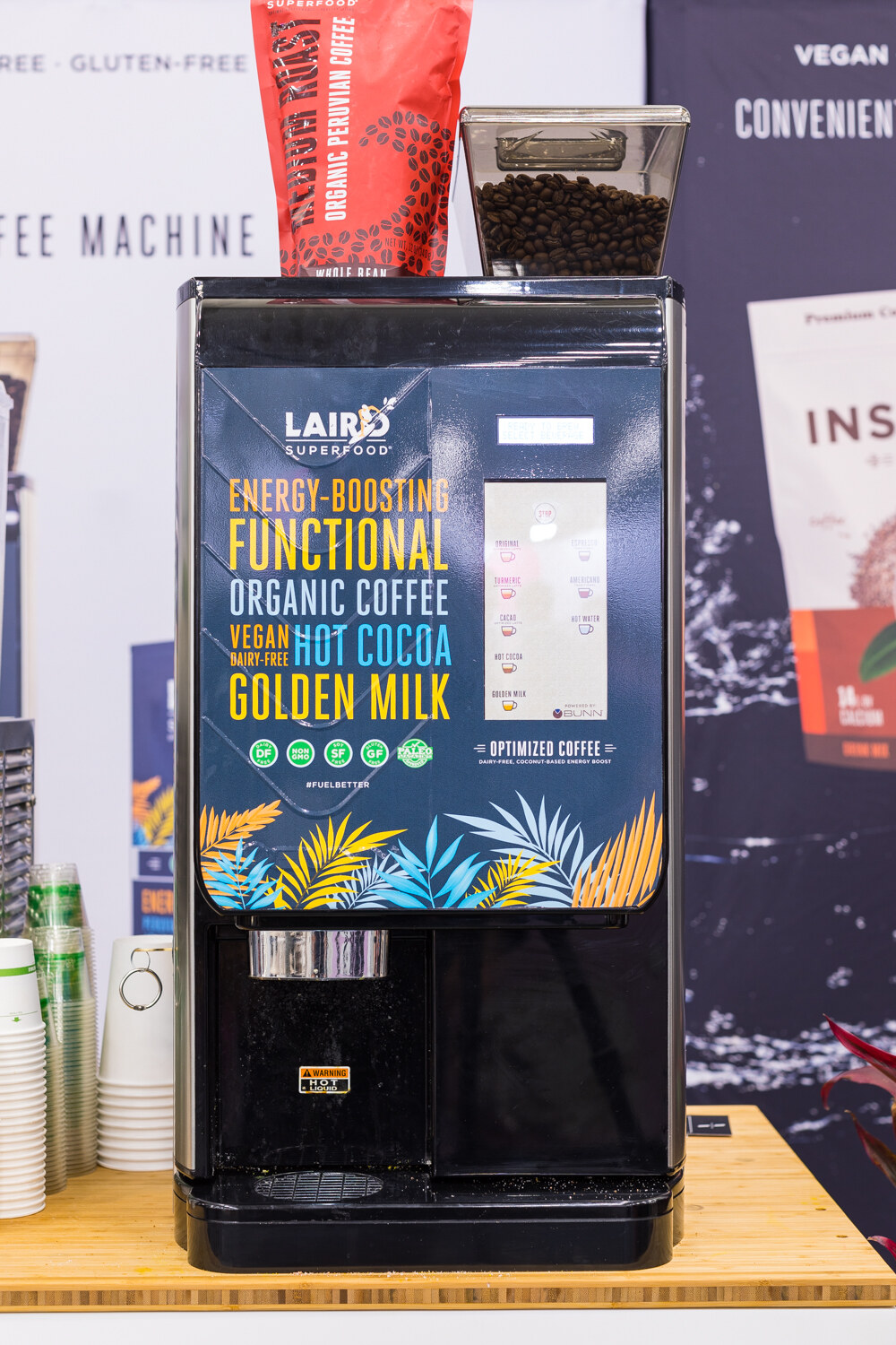 A black Laird Superfood vending-style coffee machine with coffee, hot cocoa and golden milk labels on a wooden counter.
