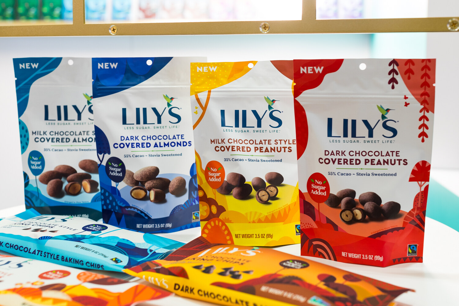 Four Lily's pouches in blue, yellow and red with baking chip bars laid out in front of them on a white table.