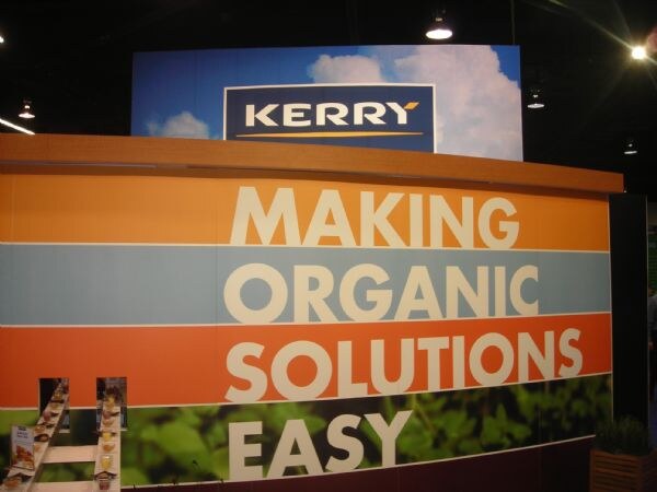 A large Kerry booth wall with the Kerry logo above orange, blue and green bands reading "Making Organic Solutions Easy." No people are visible.