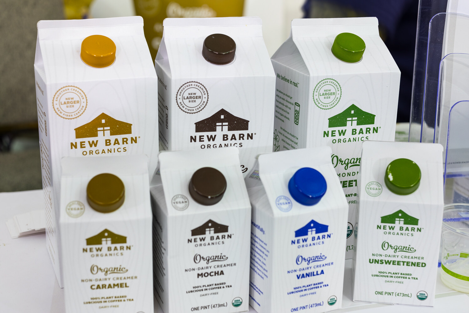 Rows of white New Barn Organics creamer cartons with colored caps in two rows on a white table.