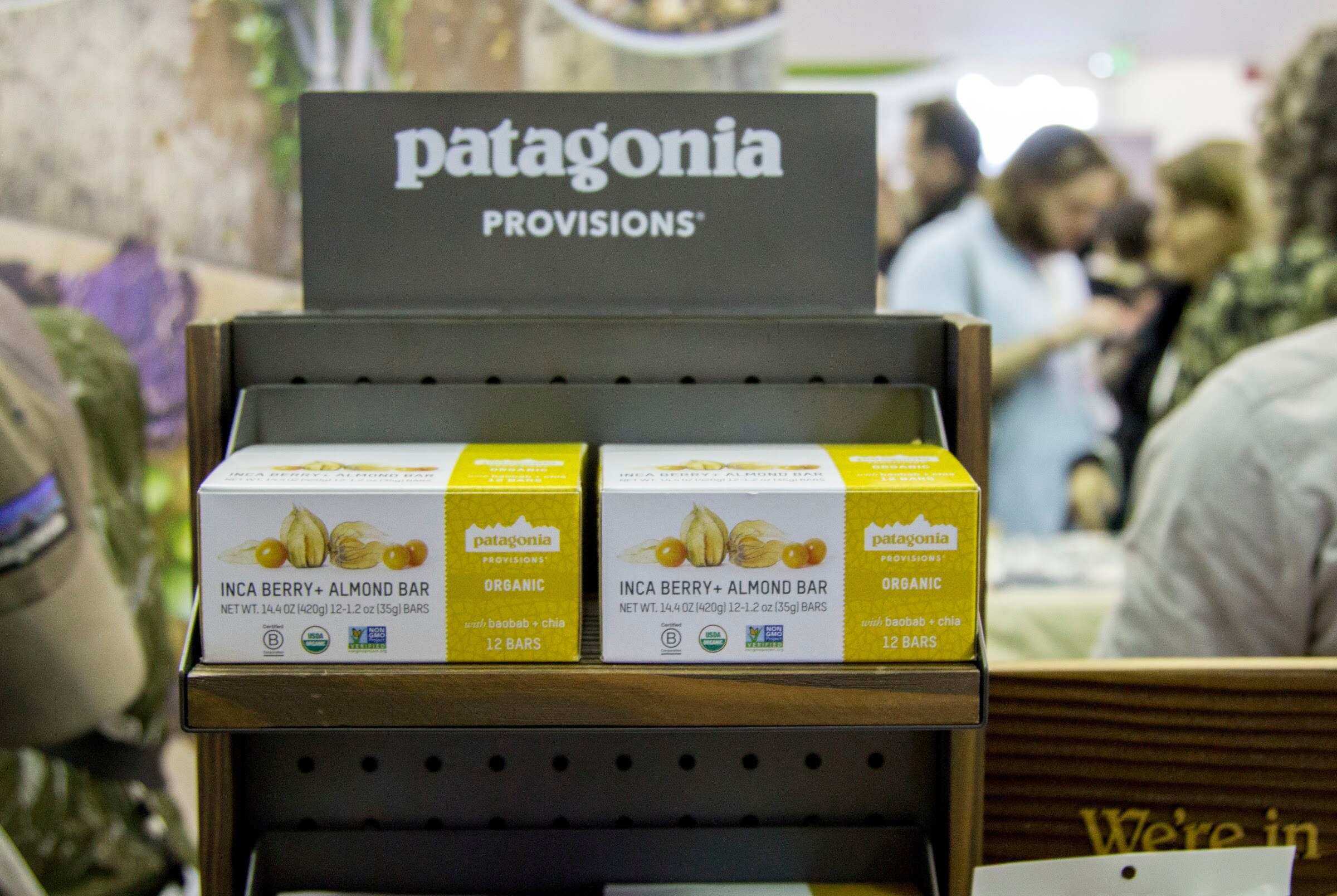 Two boxes of bars on a small wooden rack under a gray Patagonia Provisions sign with out-of-focus attendees behind.