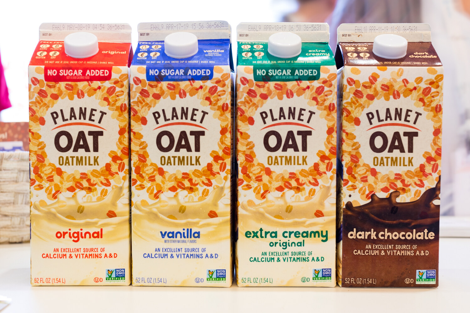 Four cartons of Planet Oat oatmilk in red, blue, green and brown labels on a white table.