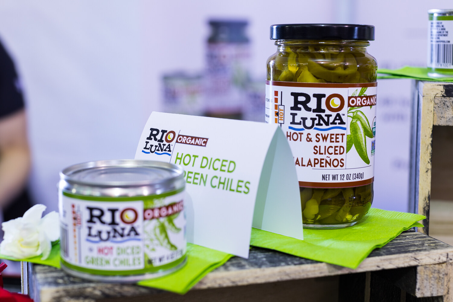 A can of Rio Luna hot diced green chiles and a jar of hot and sweet sliced jalapenos on a green napkin, with a Rio Luna table sign between them.