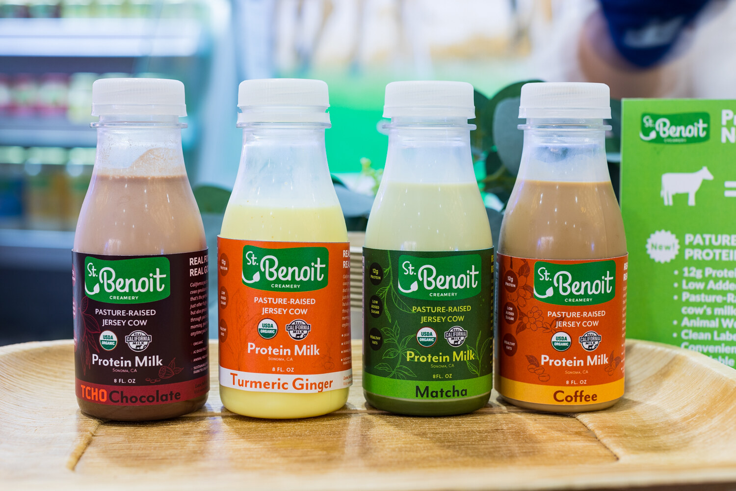 Four small bottles of St. Benoit protein milk on a wooden tray next to a green sign.