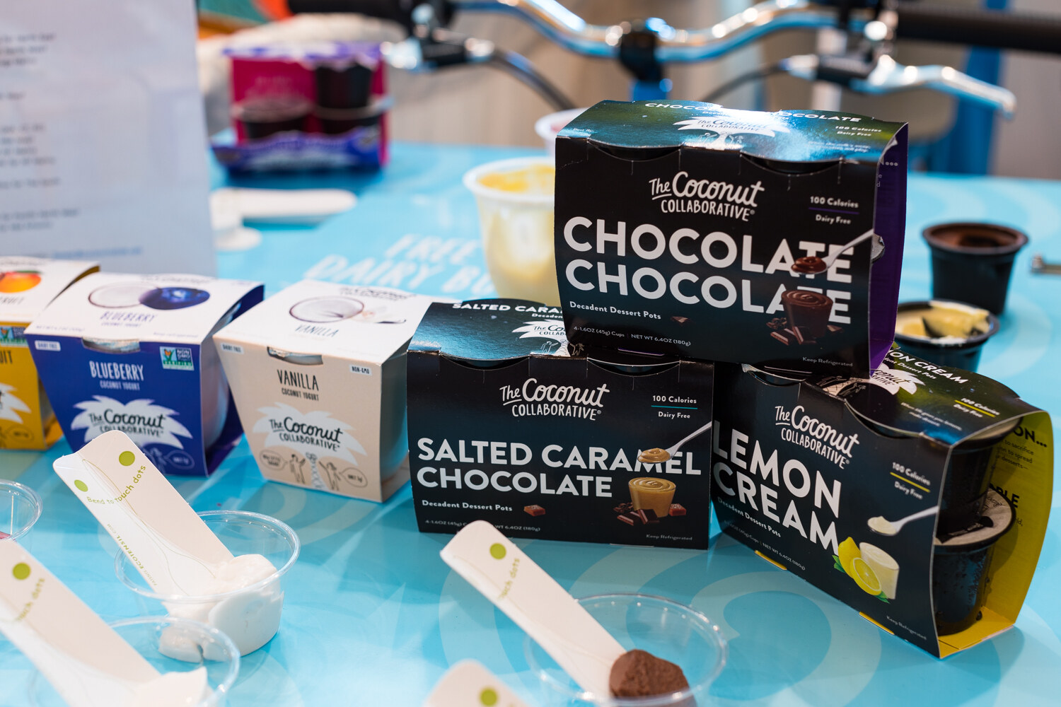 Black and white Coconut Collaborative dessert pot packs on a bright blue table with tasting spoons and small cups.