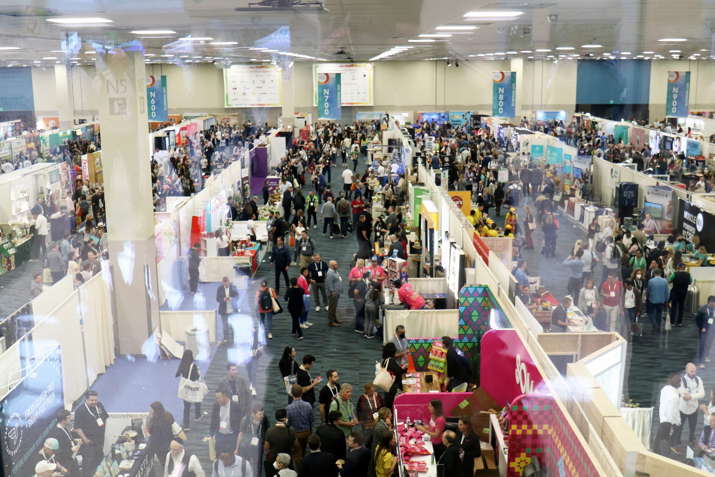 A high-angle view down onto aisles of booths crowded with attendees in an Expo West exhibit hall