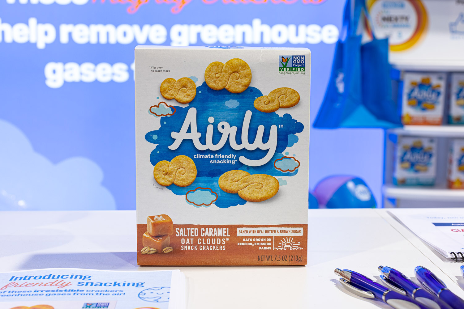 A box of Airly Salted Caramel Oat Clouds snack crackers sits on a white table in front of a blue Airly booth wall
