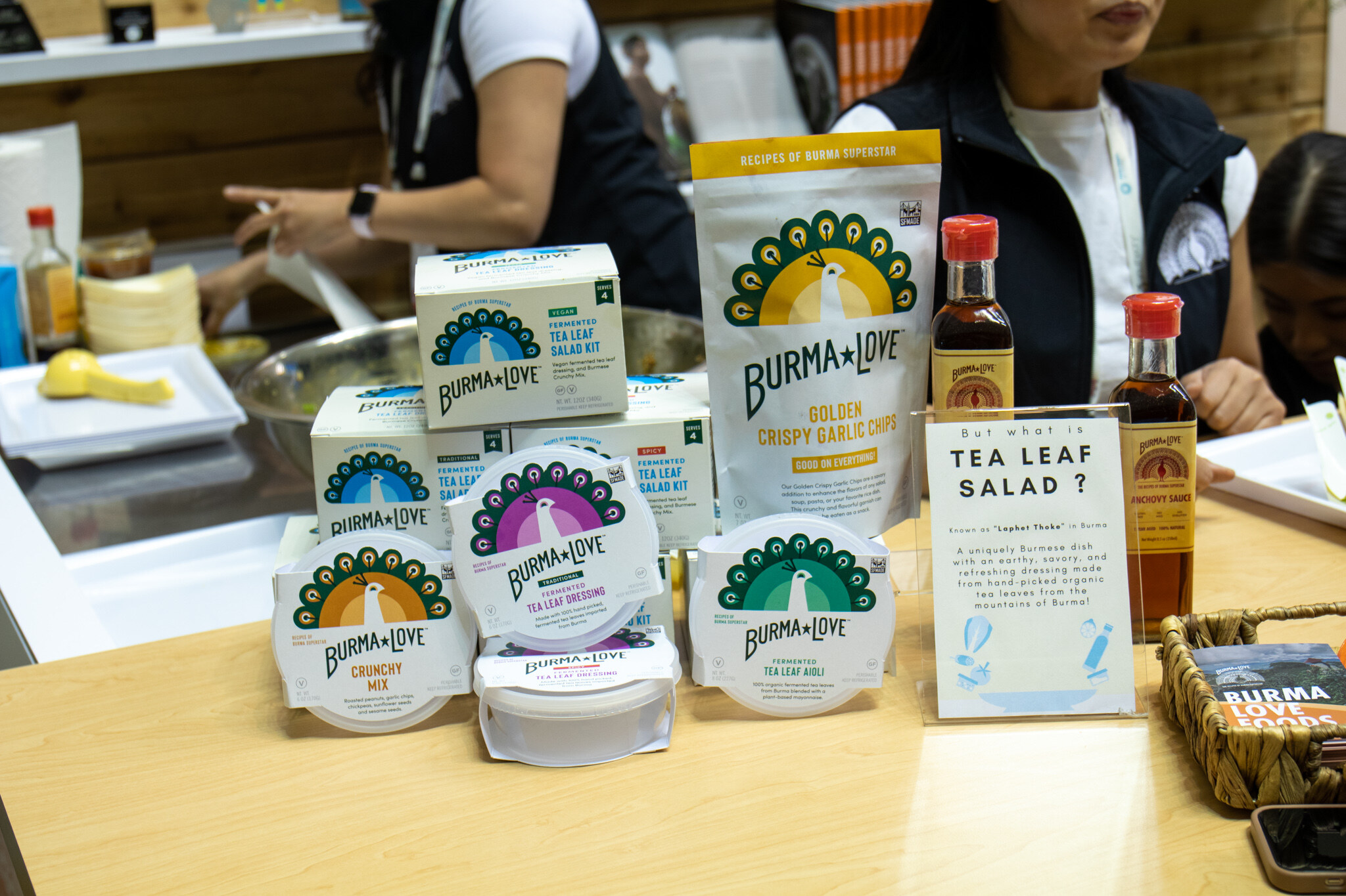 Burma Love tea leaf salad kits, crispy garlic chips and sauces sit on a counter beside a sign asking what is tea leaf salad