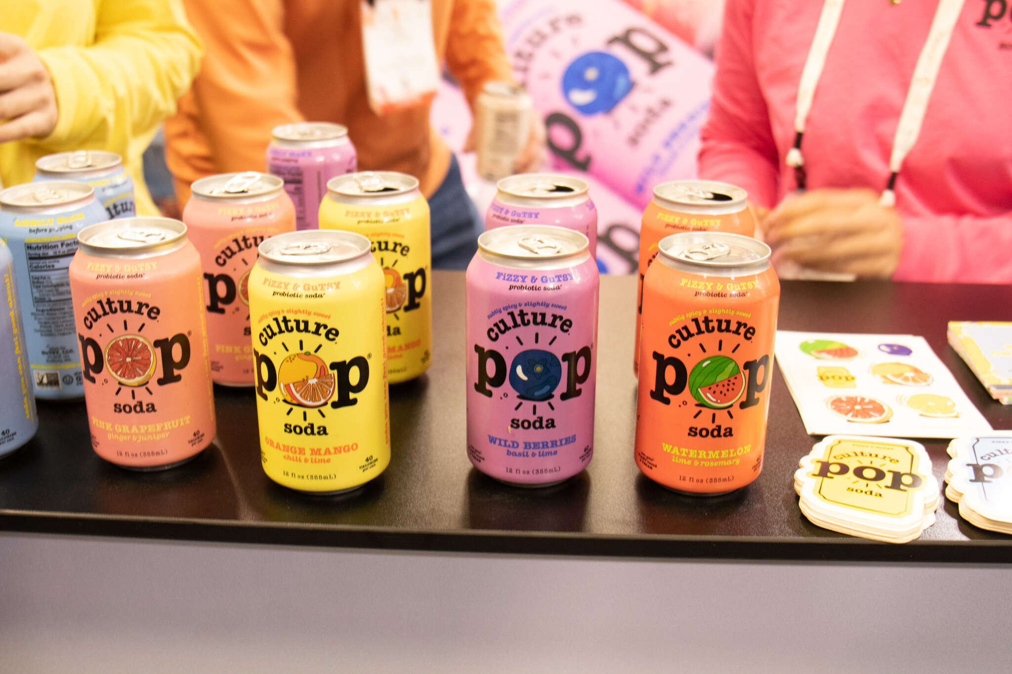 Cans of Culture Pop prebiotic soda in several flavors stand on a black counter with Culture Pop stickers