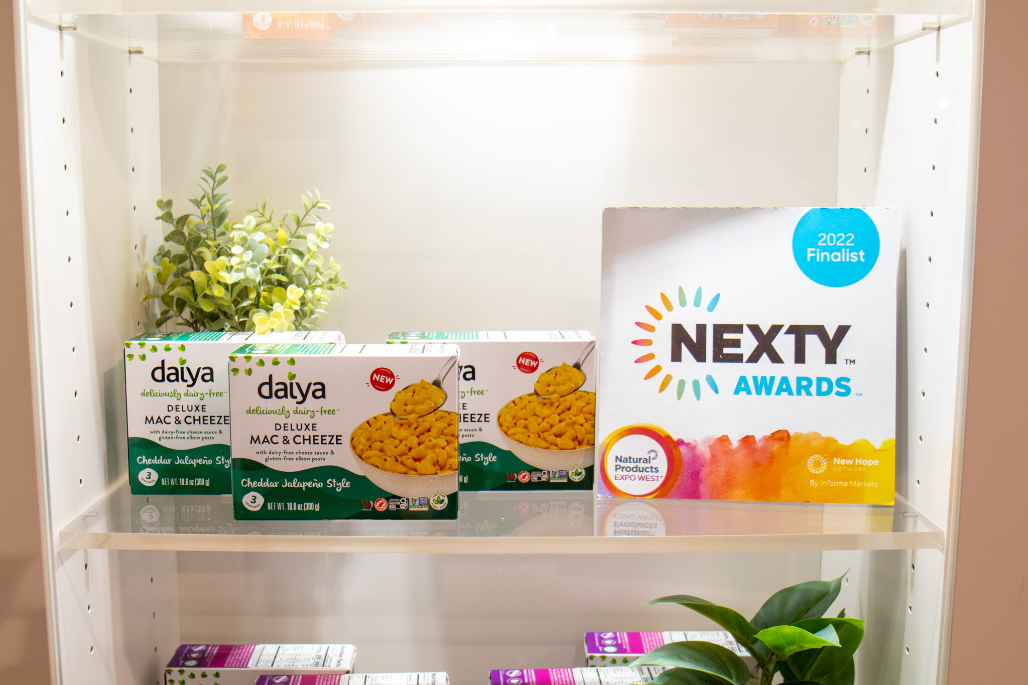 Boxes of Daiya Deluxe Mac and Cheeze sit on a white shelf next to a Nexty Awards 2022 finalist sign