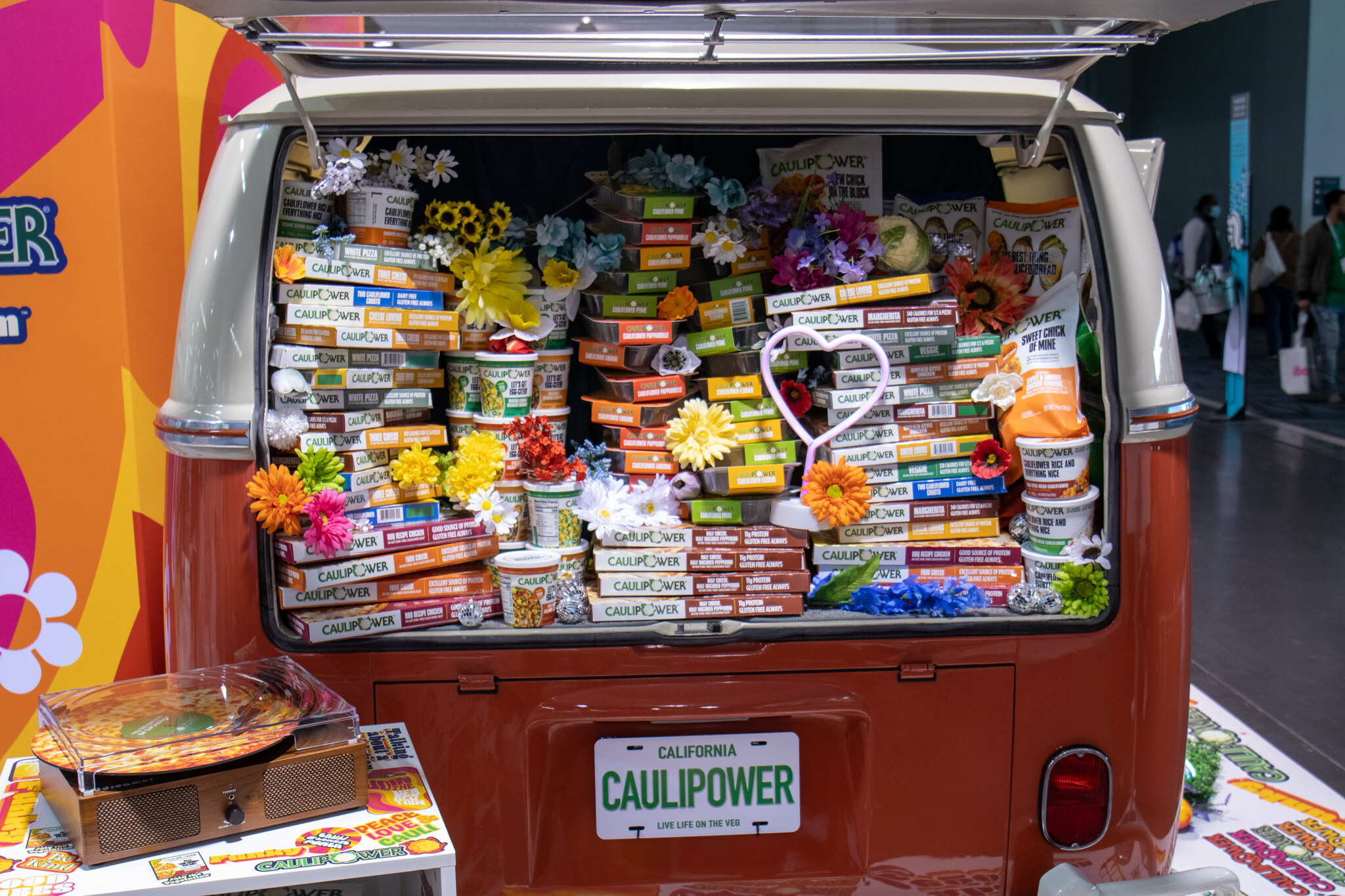 The open rear of an orange van filled with Caulipower boxes and colorful flowers with a California Caulipower license plate