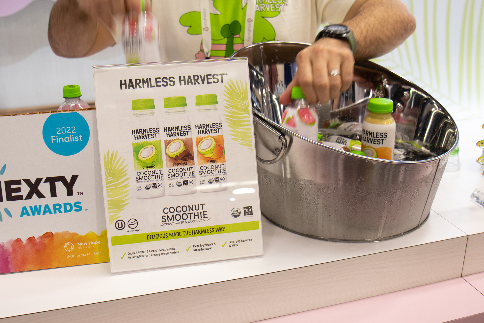 A tub of ice with Harmless Harvest coconut smoothies sits next to a sign marking a 2022 Nexty Awards finalist