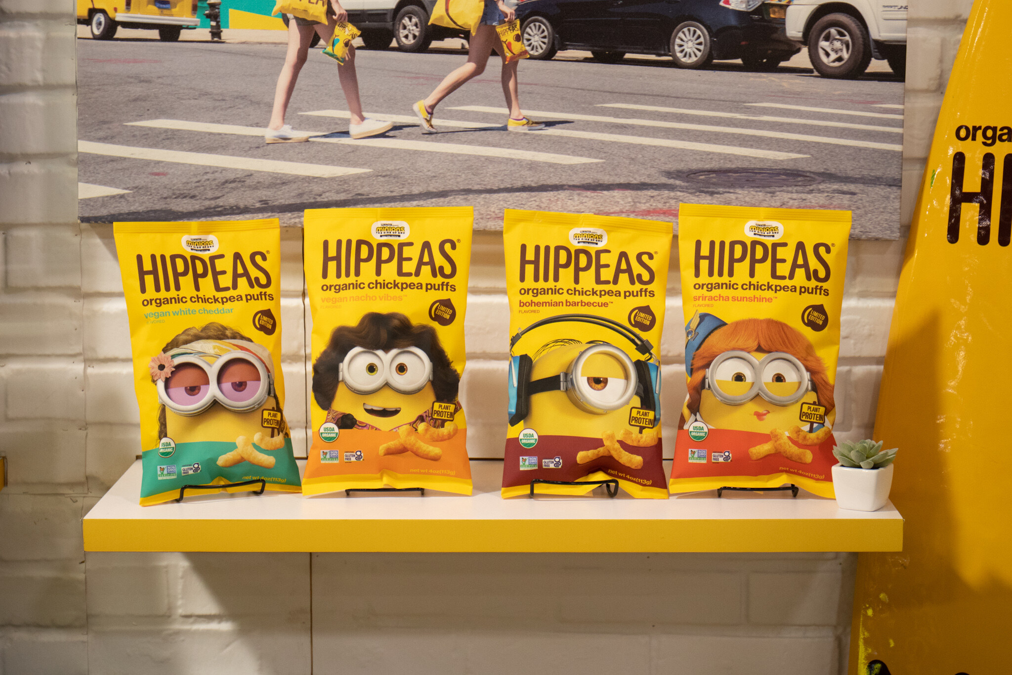 Four bags of Hippeas organic chickpea puffs with cartoon character art stand on a yellow shelf