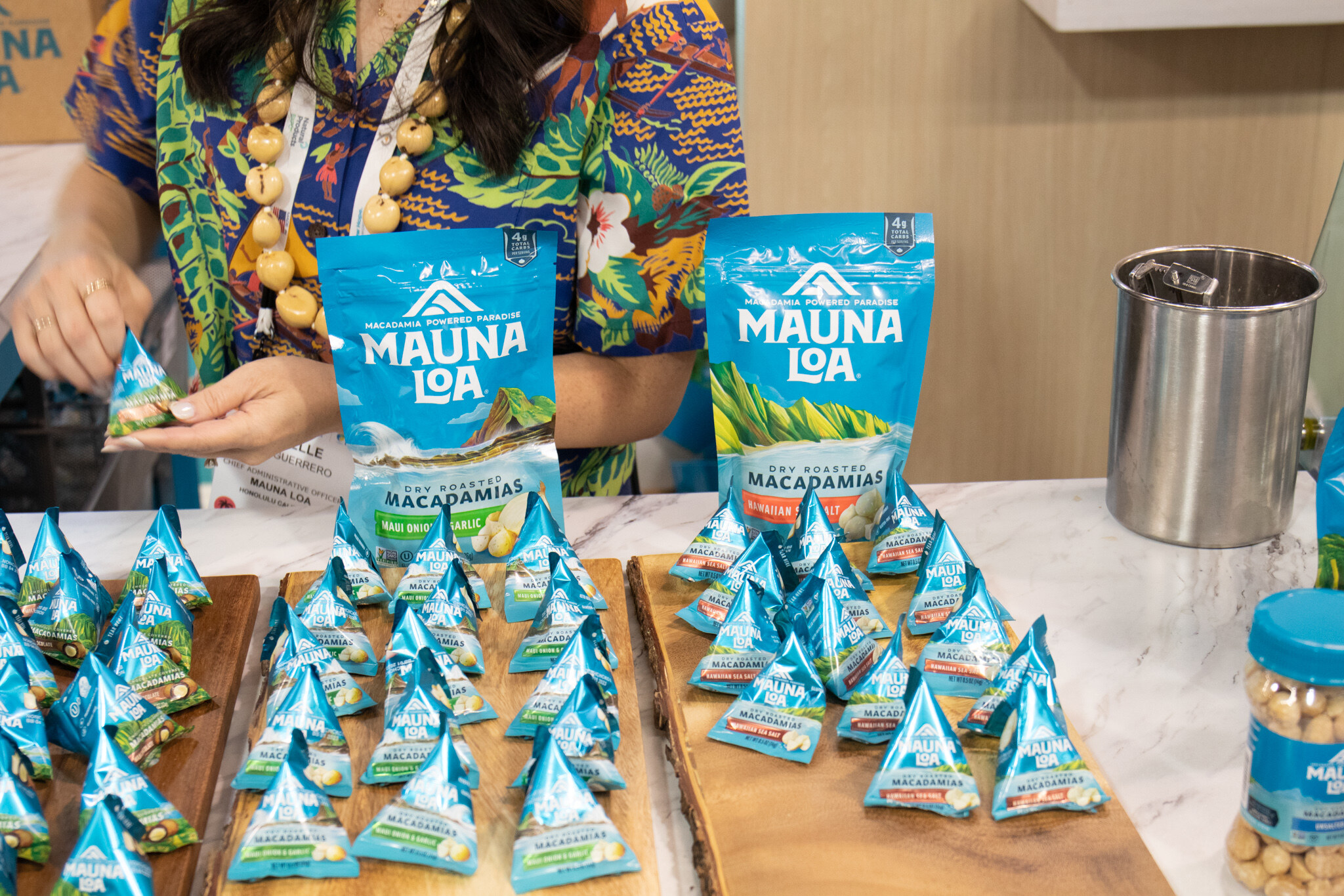 A staff member in a Hawaiian-print shirt unwraps a sample of Mauna Loa macadamia nuts among bags and individually wrapped samples on wooden boards