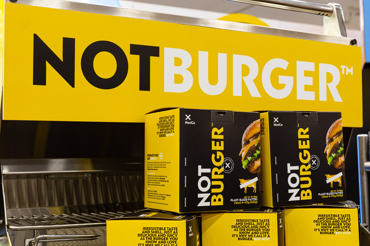 Stacked boxes of NotBurger plant-based patties sit under a large yellow NotBurger sign