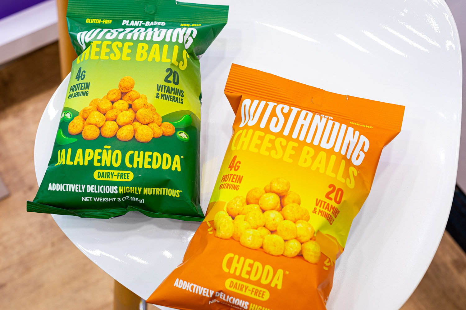 Two bags of Outstanding Cheese Balls, Jalapeno Cheddar and Cheddar, lie on a white table