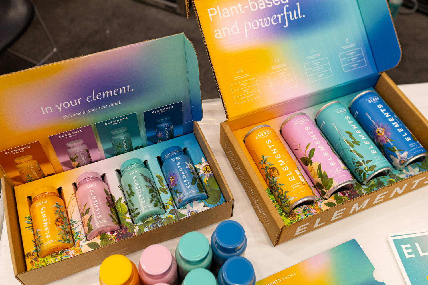 An open gradient-colored box holding four tall Elements cans