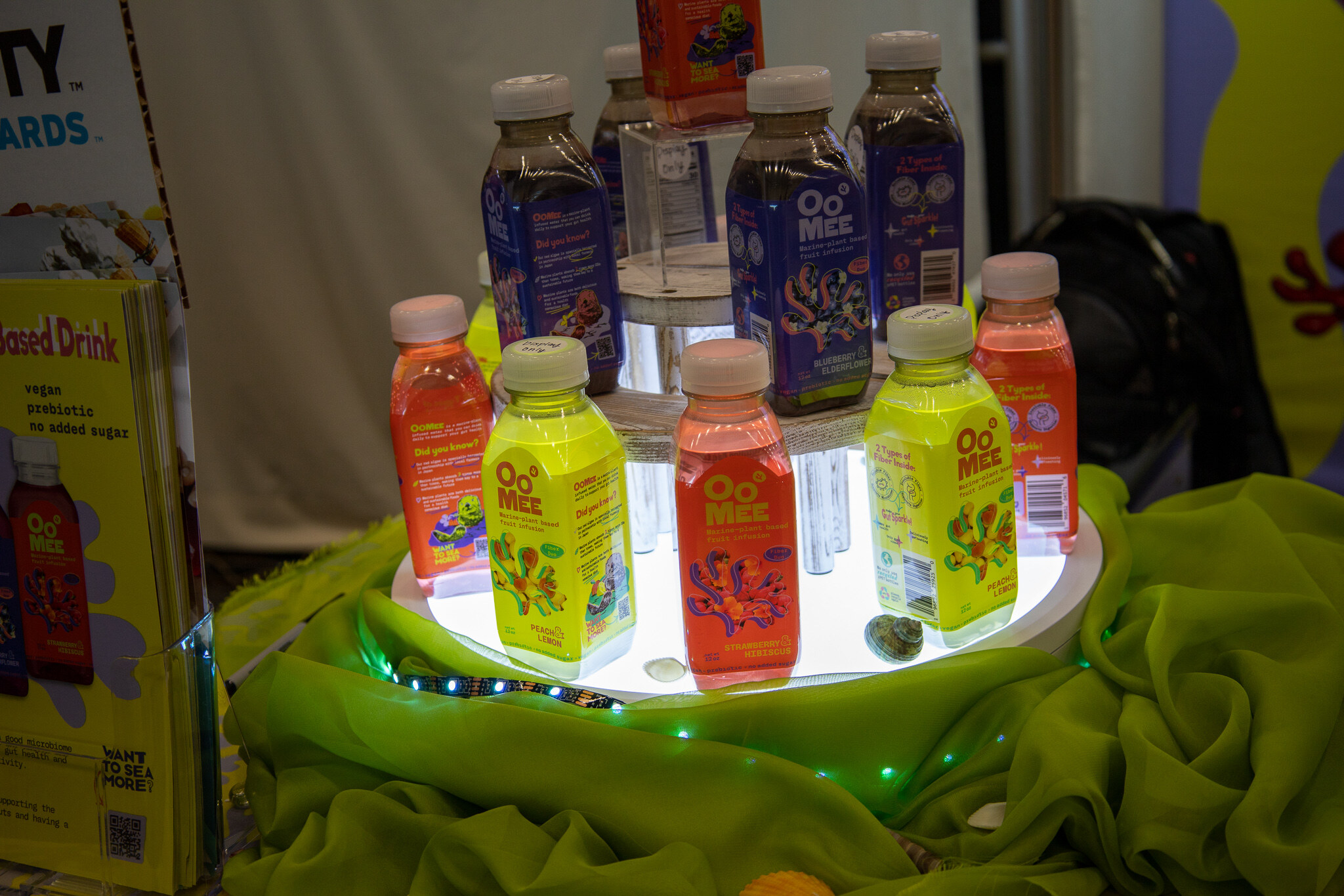 A lit round display of colorful juice bottles on a green drape beside a Nexty Awards sign