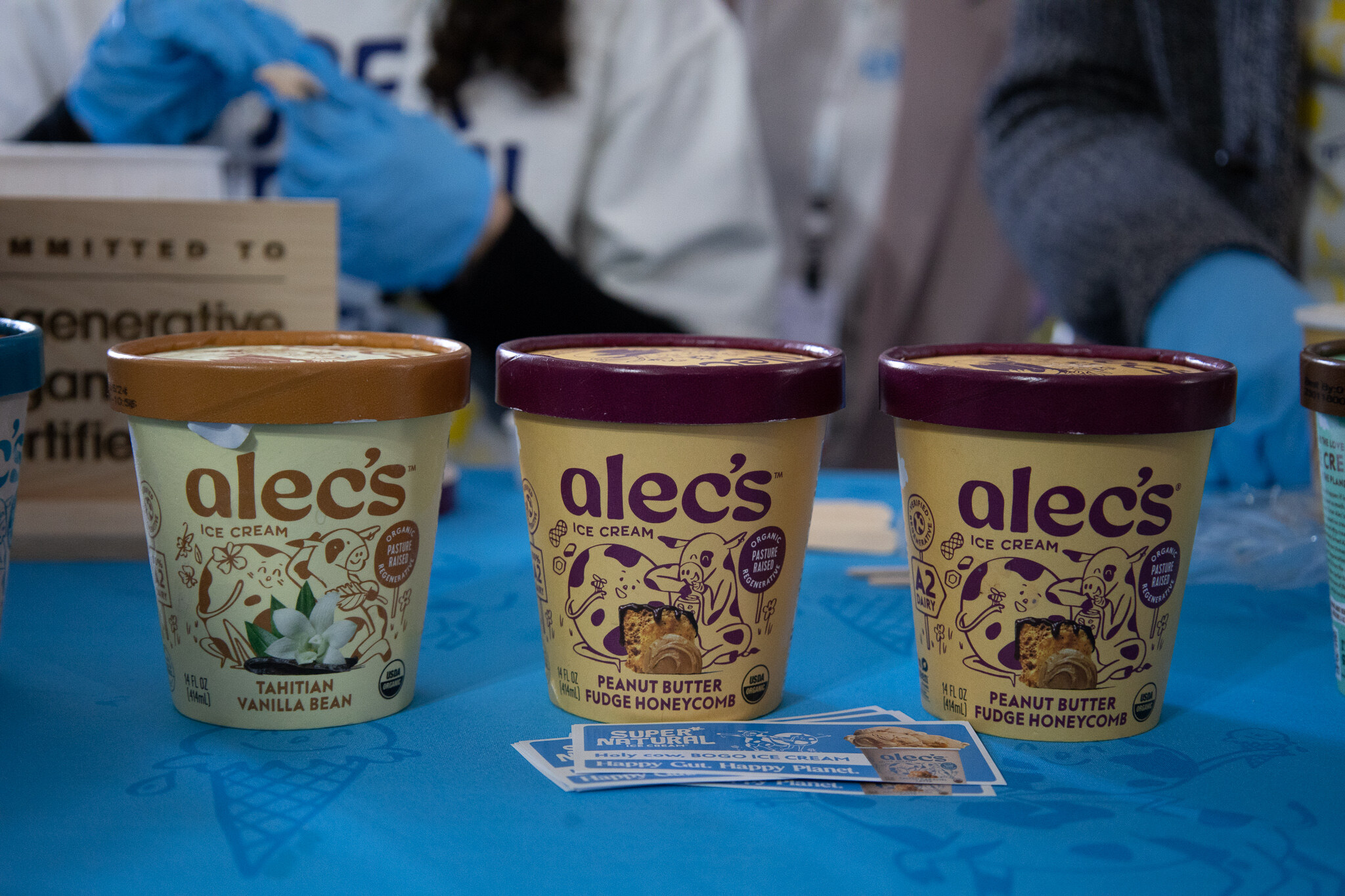 Three Alec's Ice Cream pints on a blue table at a sampling booth