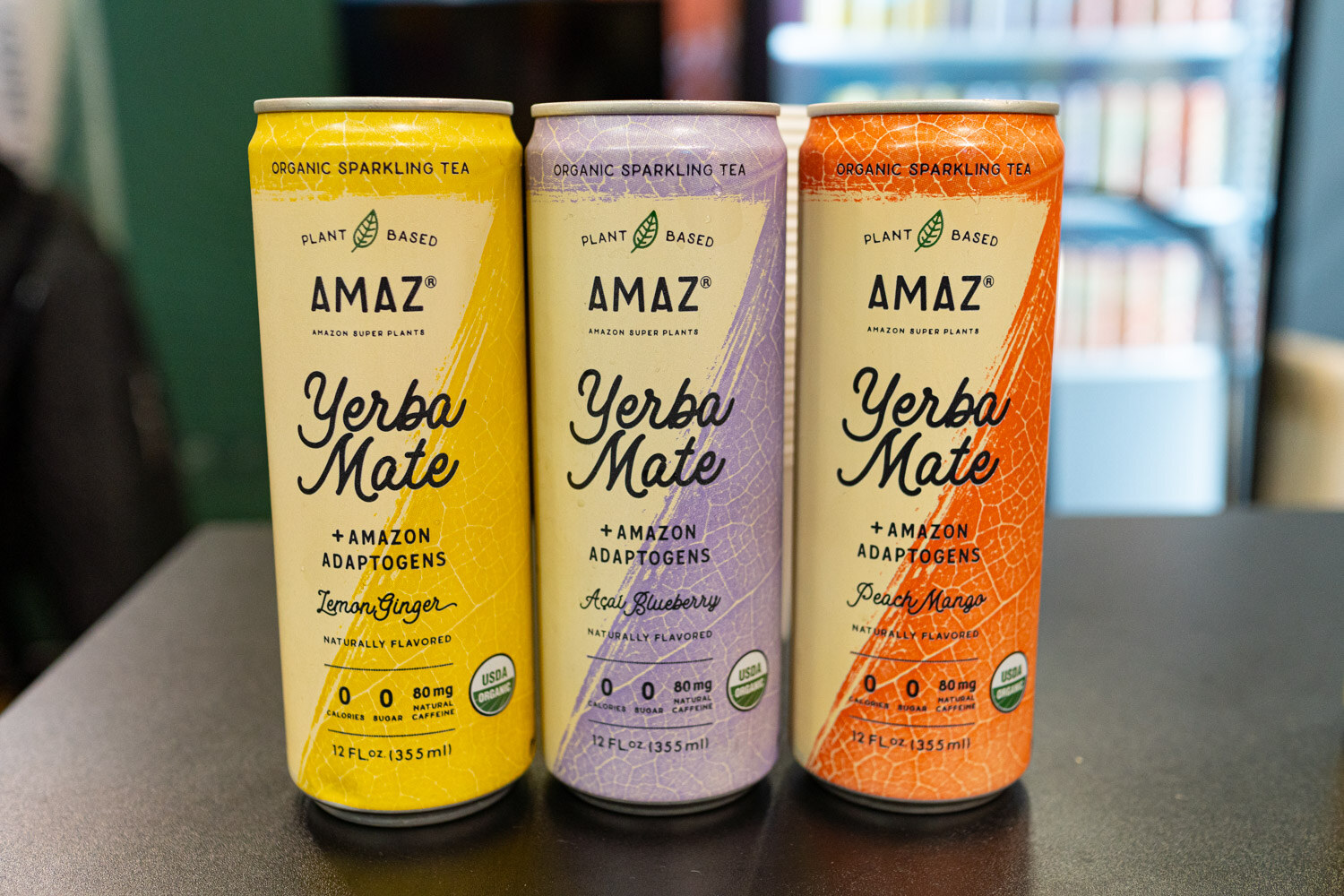 Three Amaz organic sparkling yerba mate cans in yellow, lavender and orange