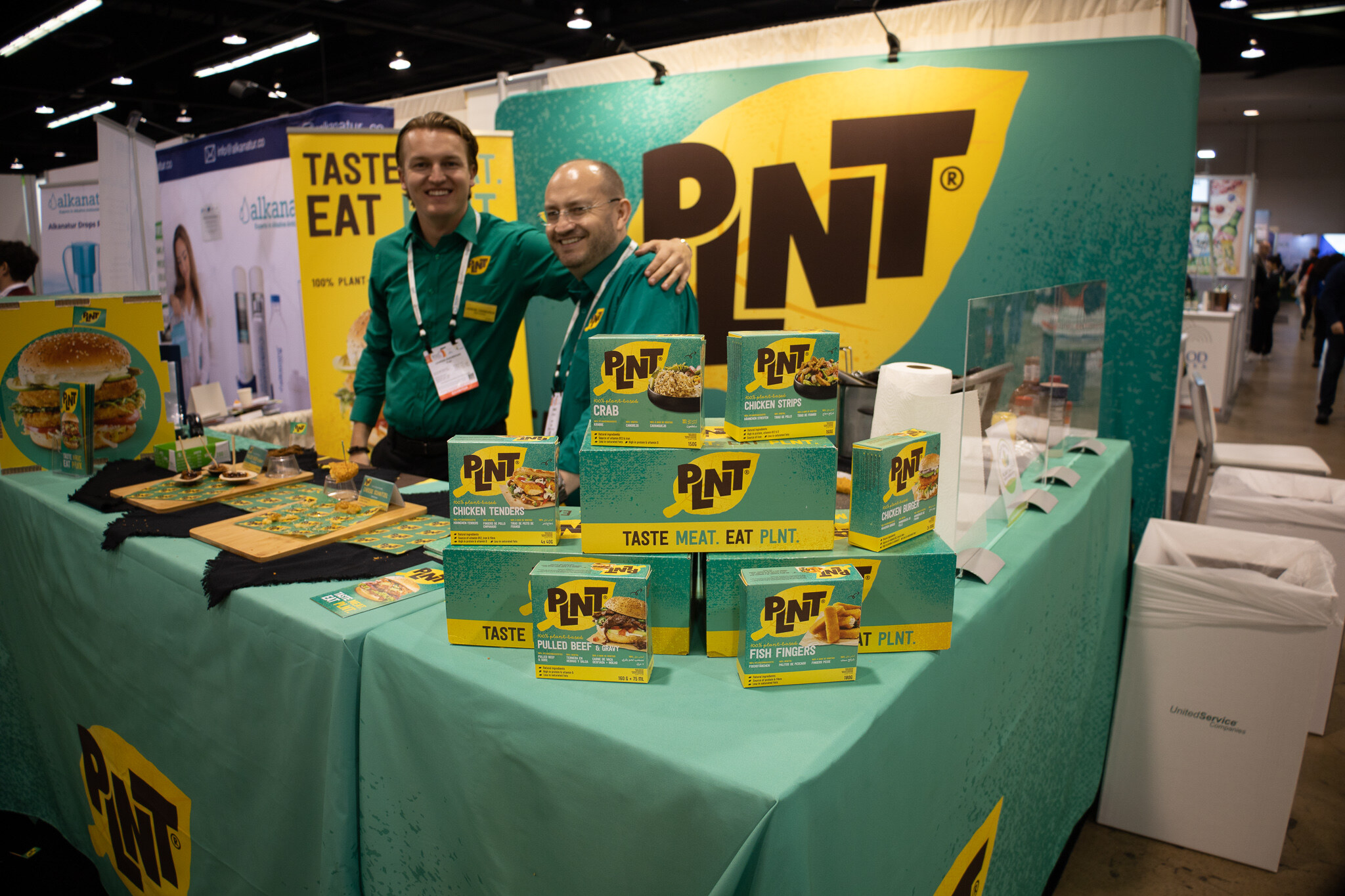 Two people stand behind a teal table stacked with PNT boxes