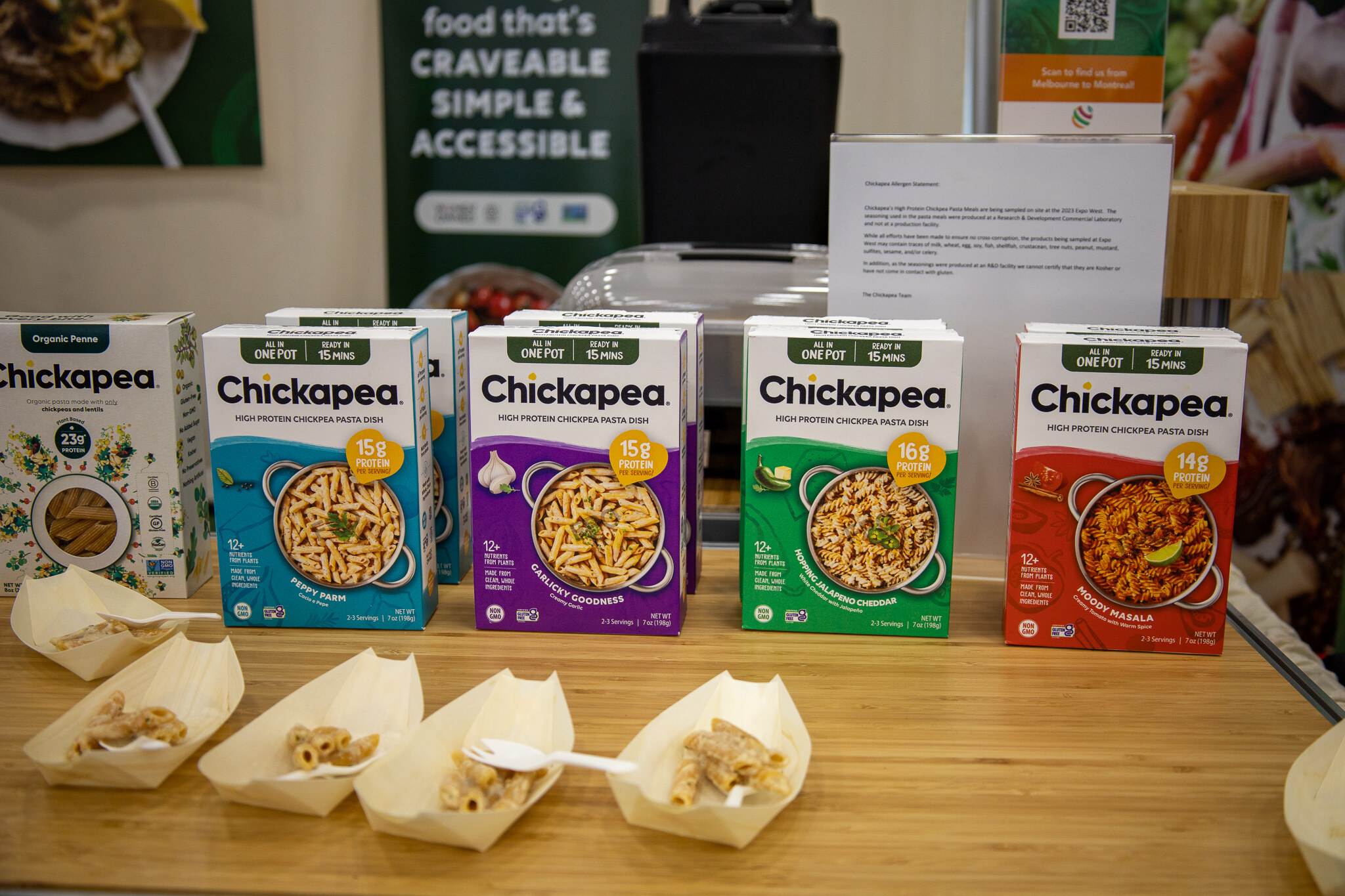 A row of Chickapea pasta boxes above trays of sample cups on a wooden counter