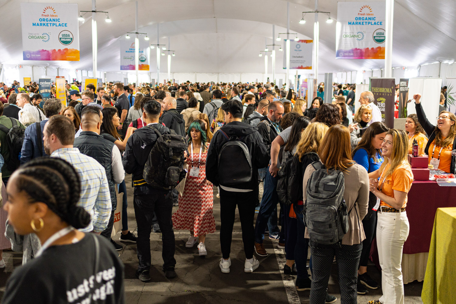 A dense crowd of attendees walking through a large tent between booths