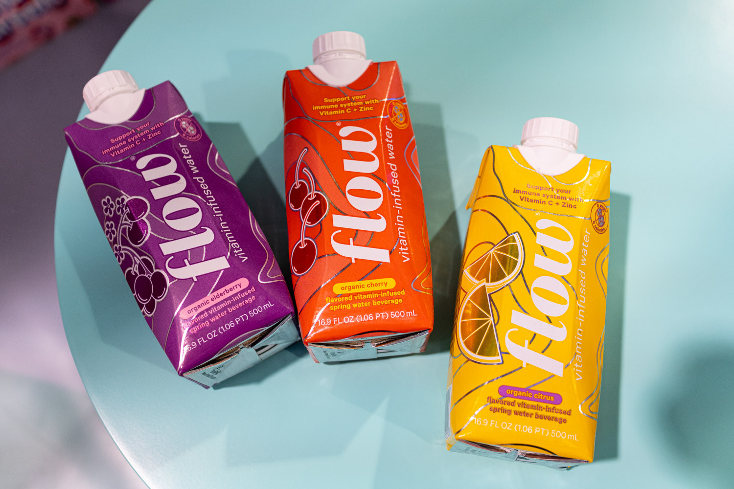 Three Flow water cartons in purple, orange and yellow on a teal table
