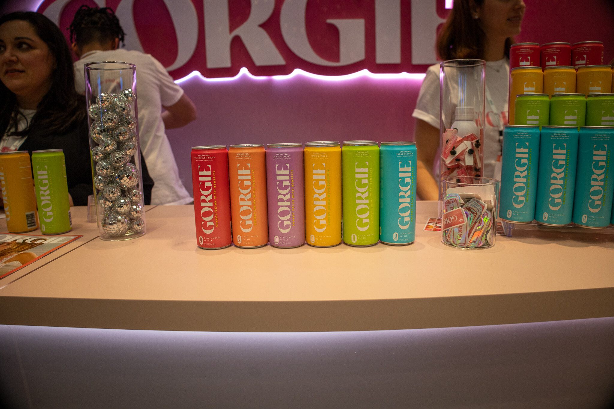 A row of colorful Gorgie cans on a pink counter in front of a candy jar