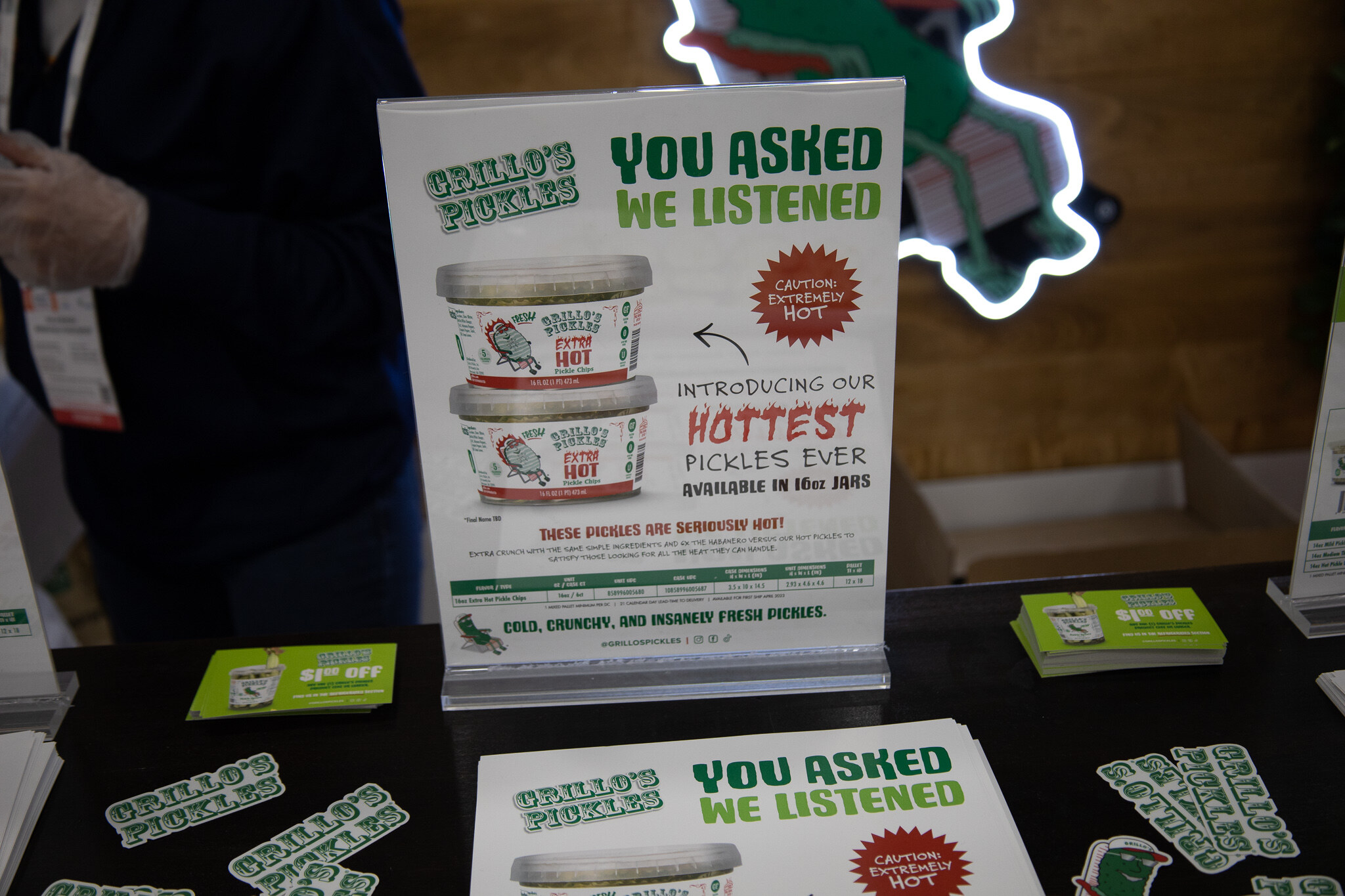 Grillo's Pickles signage and stickers on a black counter with a sign reading You Asked We Listened