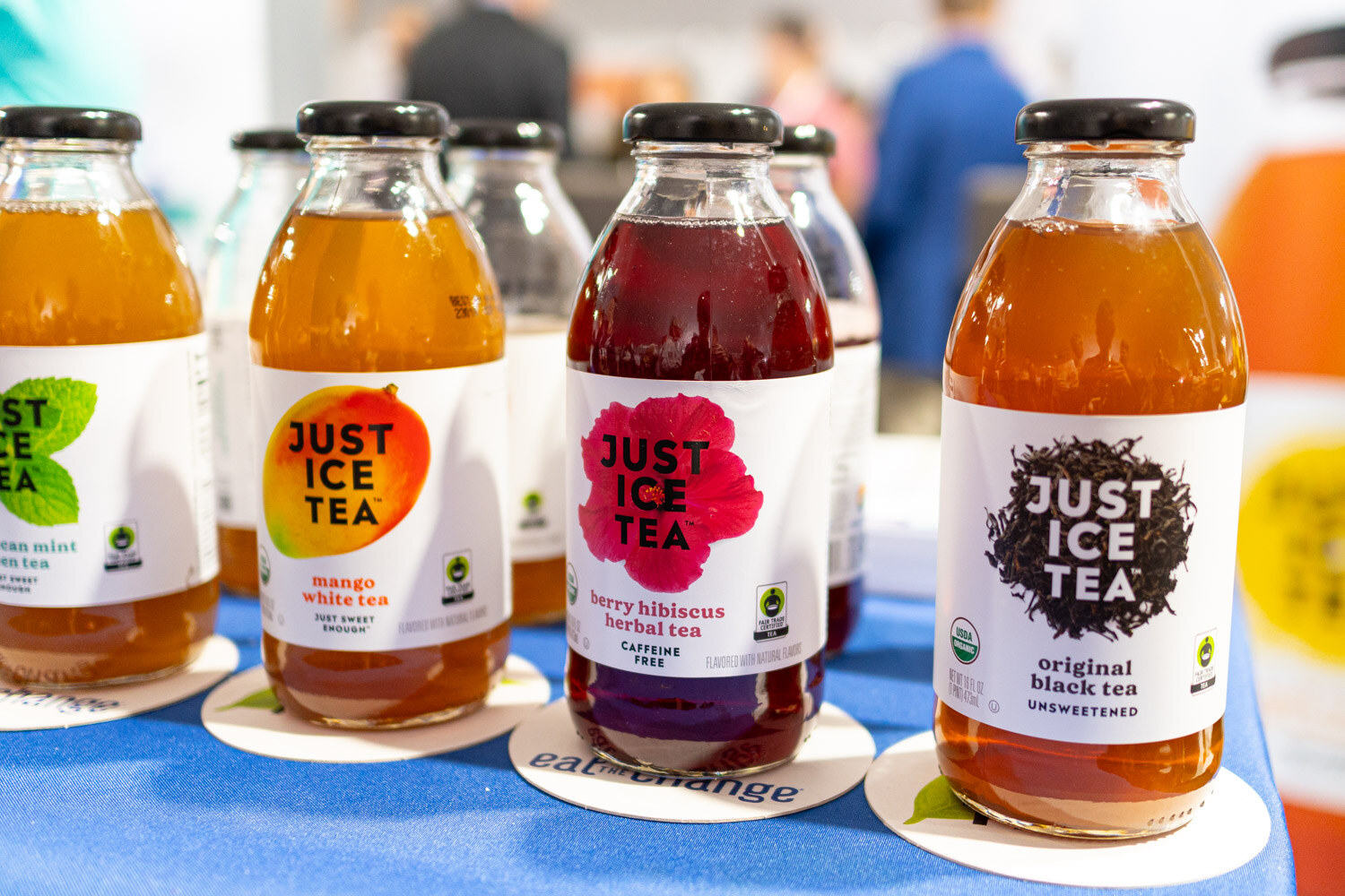 Four Just Ice Tea glass bottles in mango, hibiscus, peach and black tea flavors on a blue tablecloth