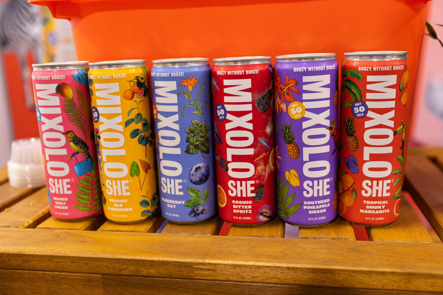 A row of tall colorful Mixoloshe cans on a wooden counter
